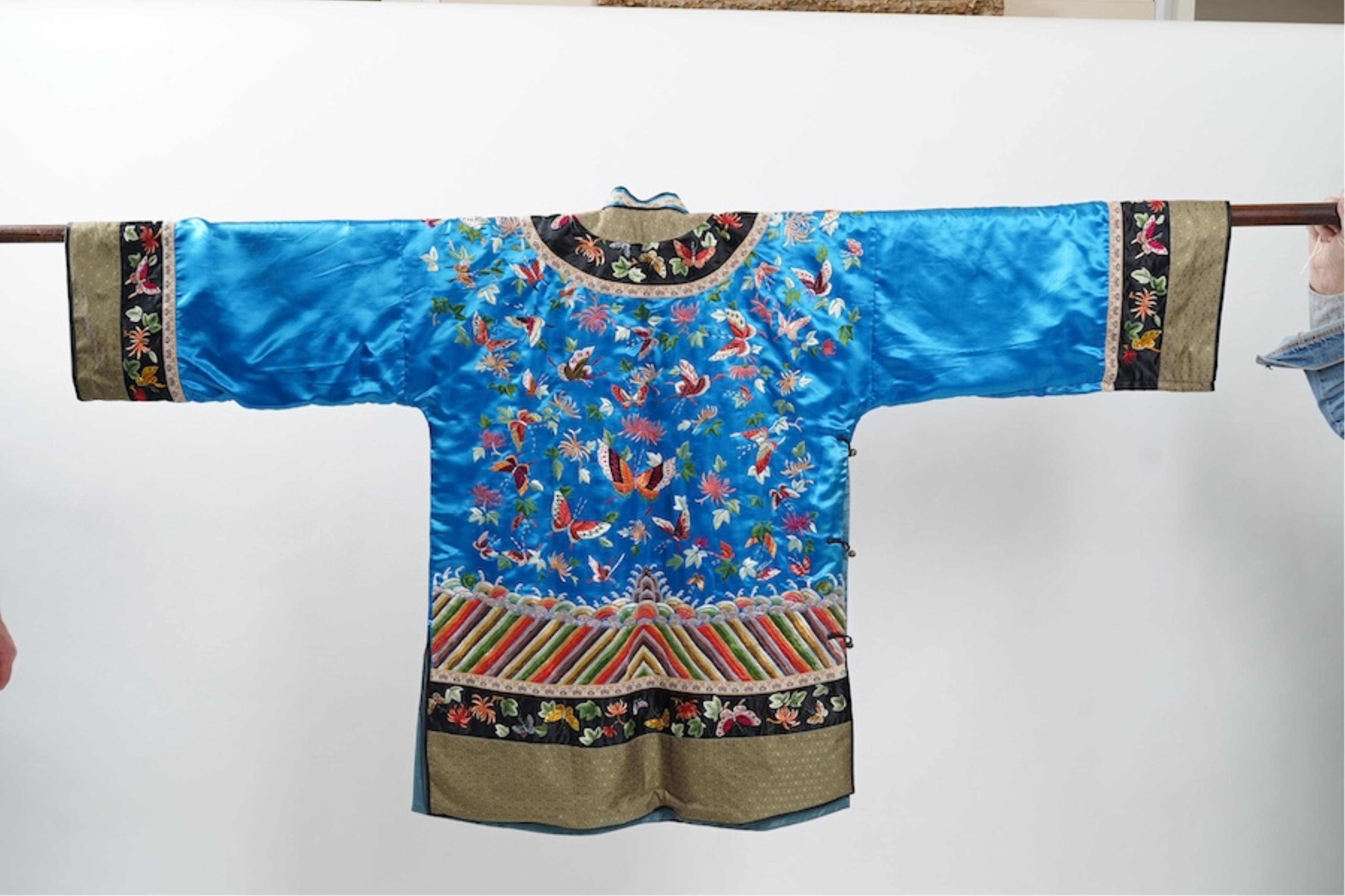 A mid 20th century Chinese turquoise silk jacket, with all over polychrome butterfly embroidery, similar embroidered sleeve bands, front and bottom edges on black silk, all bordered with gold brocade. The jacket blue sil